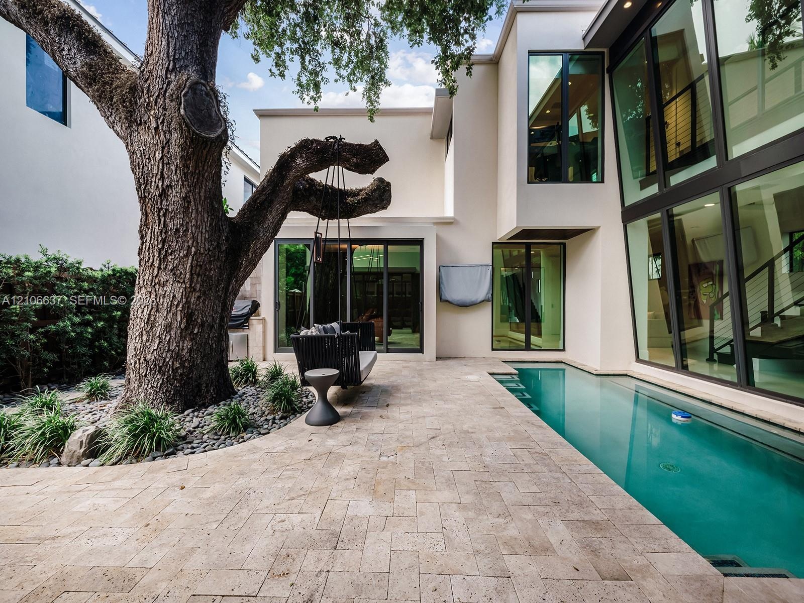 Modern architectural exterior featuring expansive floor-to-ceiling glass windows, a custom geometric lap pool, herringbone-patterned stone decking, an