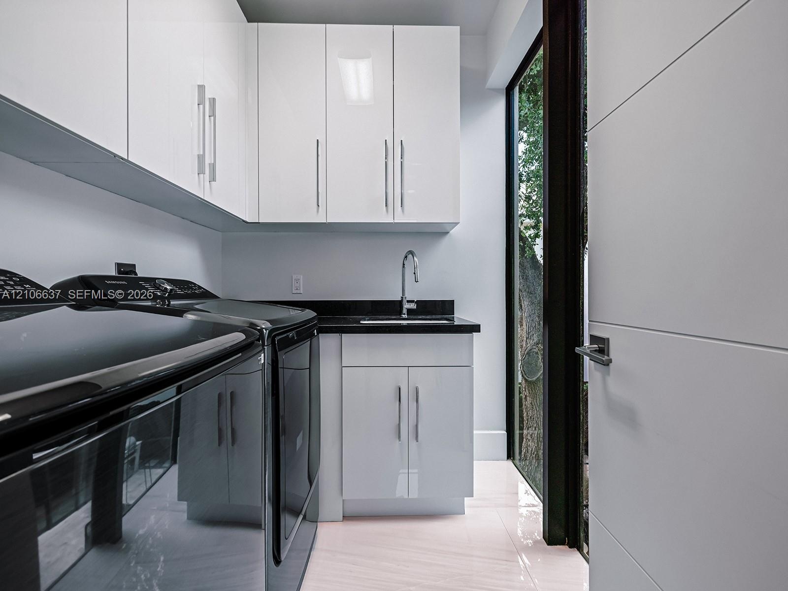 Glossy white cabinetry with vertical pulls, solid-surface dark countertop, undermount sink with gooseneck faucet, light-toned polished flooring, and f