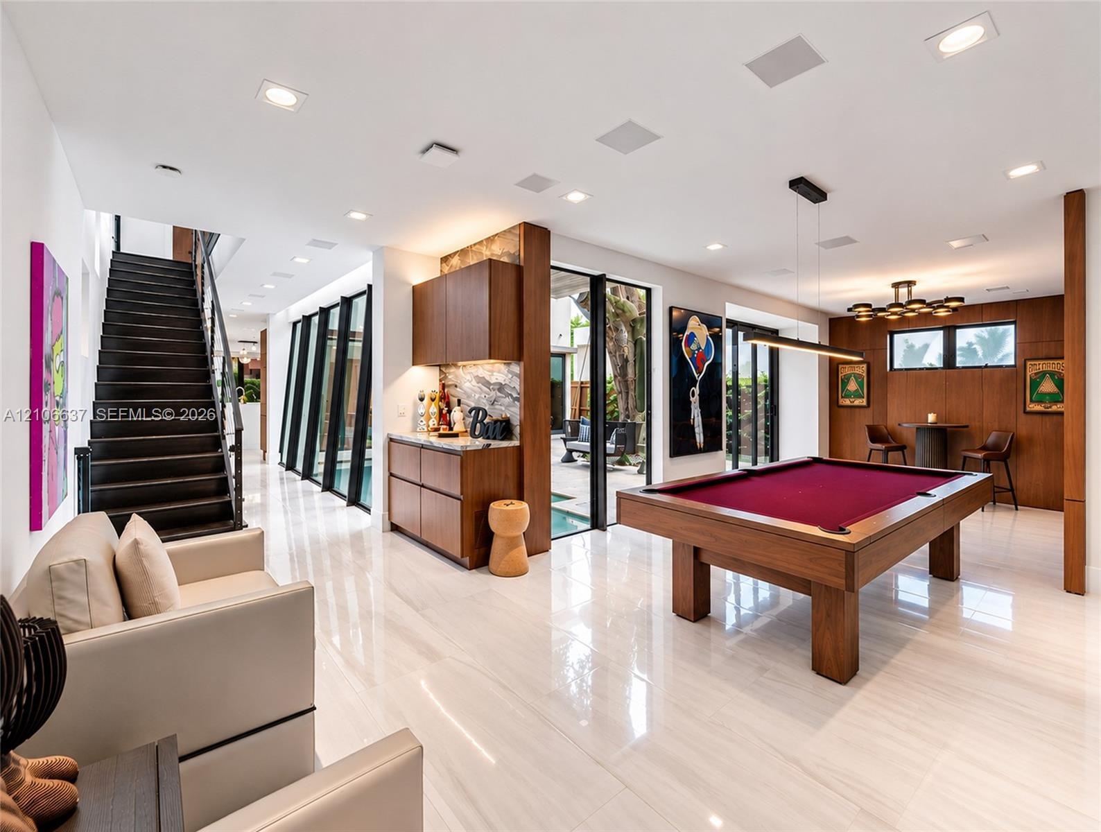 Polished stone flooring, wood-panelled accent walls, integrated bar cabinetry with stone backsplash, staircase with open risers, and floor-to-ceiling 