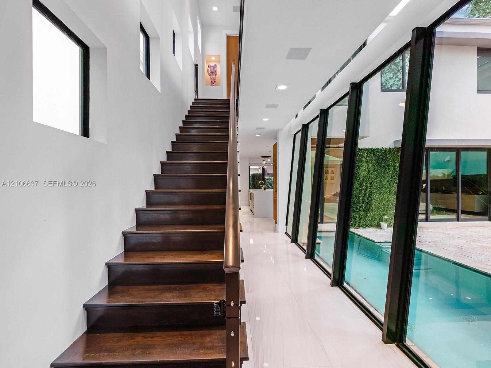 Staircase featuring dark wood treads and a linear handrail, large-format tile flooring, recessed ceiling lighting, and floor-to-ceiling glass wall pan