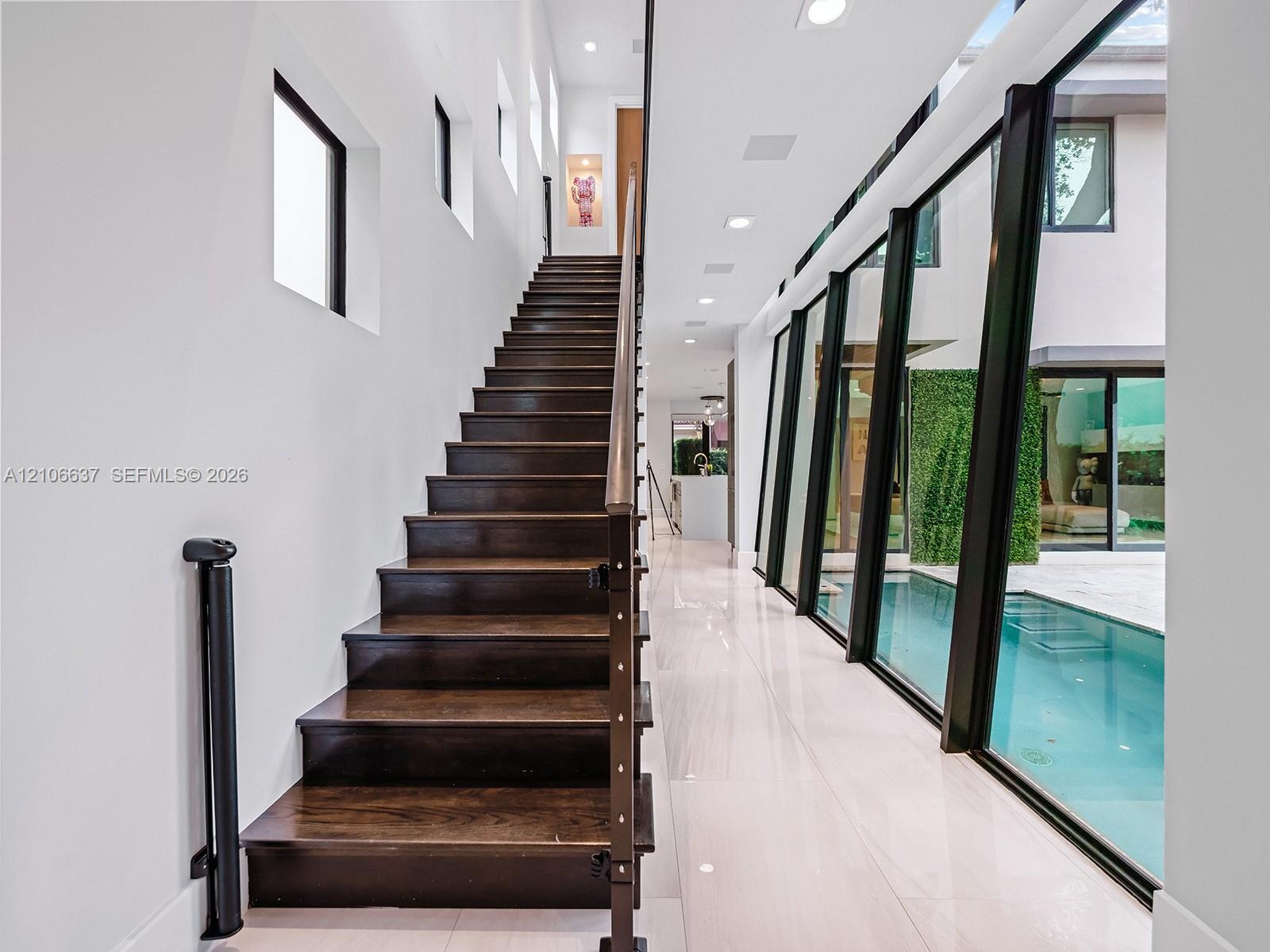 Staircase with dark wood-finish treads and metal railings, large-format tile flooring, recessed ceiling lighting, and floor-to-ceiling black-framed wi