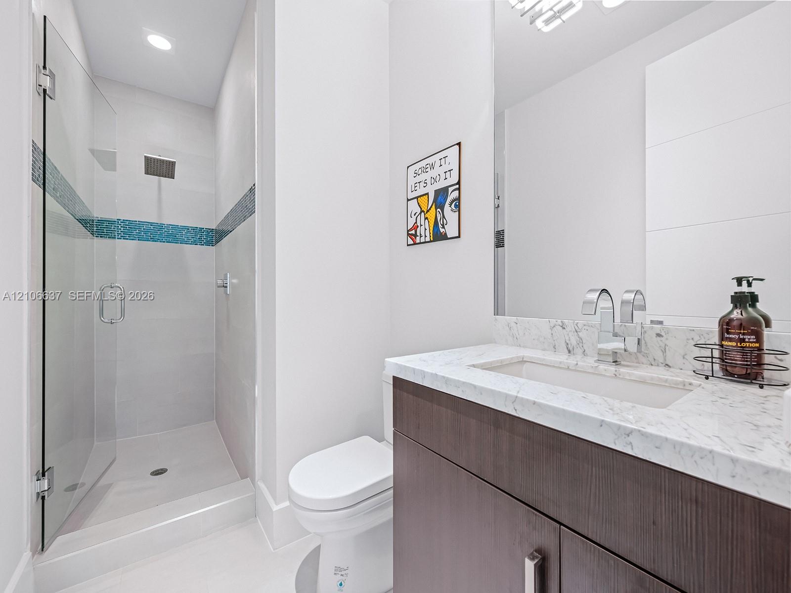 Modern bathroom featuring a dark wood-finish vanity, light-toned stone-finish countertop with an integrated rectangular sink, glass-enclosed shower wi