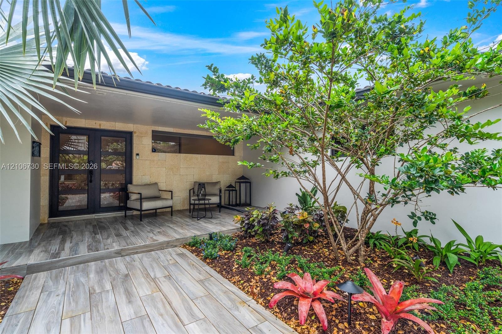 Covered entryway featuring wood-finish tile flooring, natural stone veneer exterior wall, and a double-door entry with horizontal glass panes