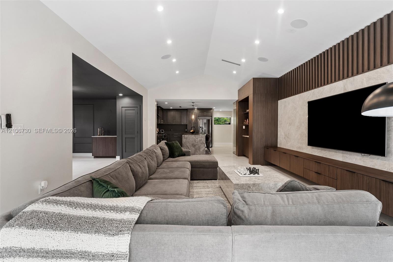 Vaulted ceiling featuring recessed lighting, stone-finish accent wall with integrated media storage, and custom floor-to-ceiling wood slat paneling