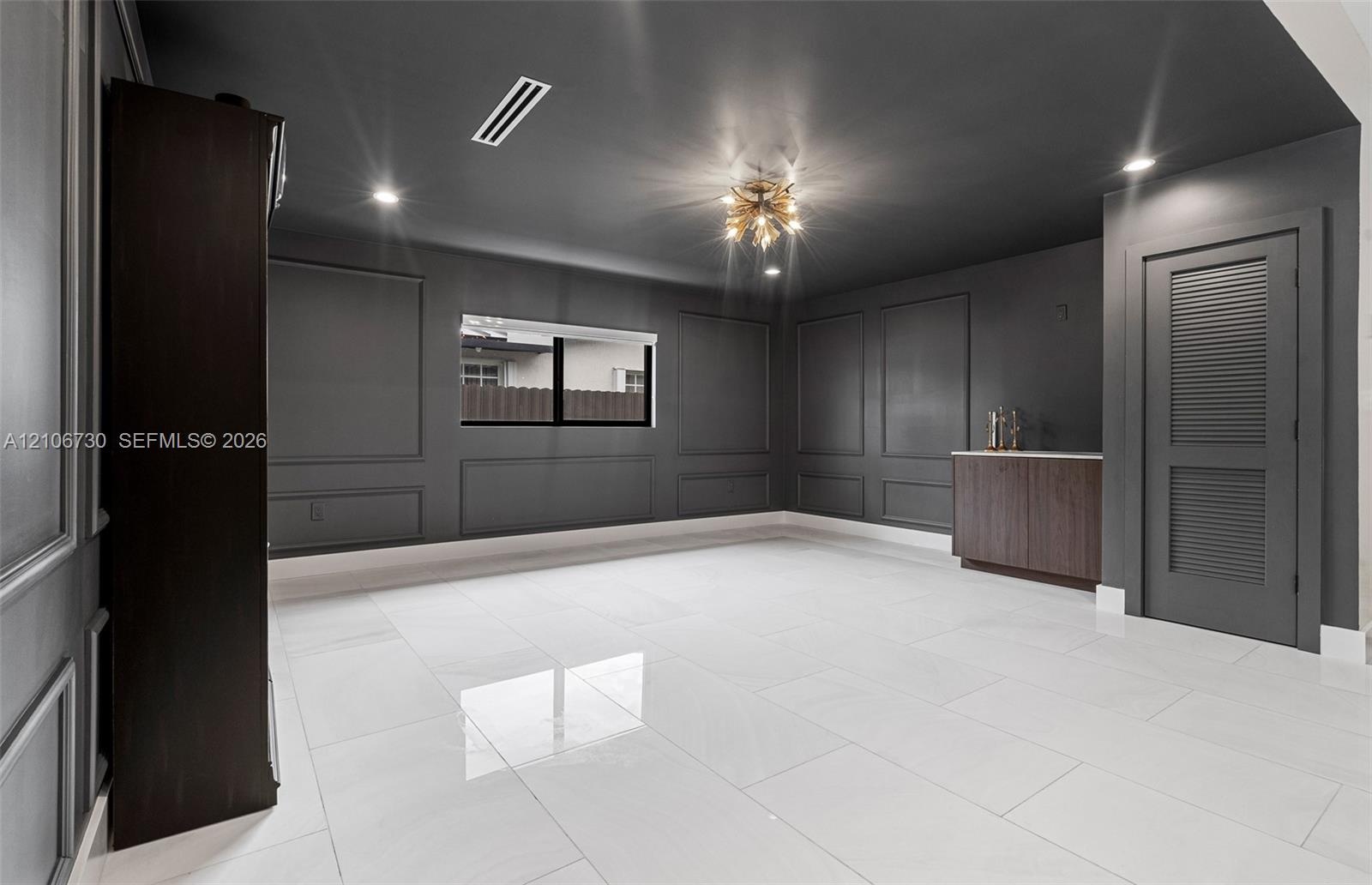 Interior space featuring charcoal-toned wall paneling, large-format polished tile flooring, a built-in wood-finish wet bar, and a multi-light flush-mo