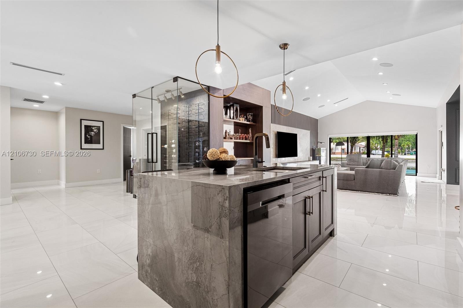 Kitchen island featuring a waterfall stone countertop, dark cabinetry, recessed lighting, and a glass-enclosed display storage unit