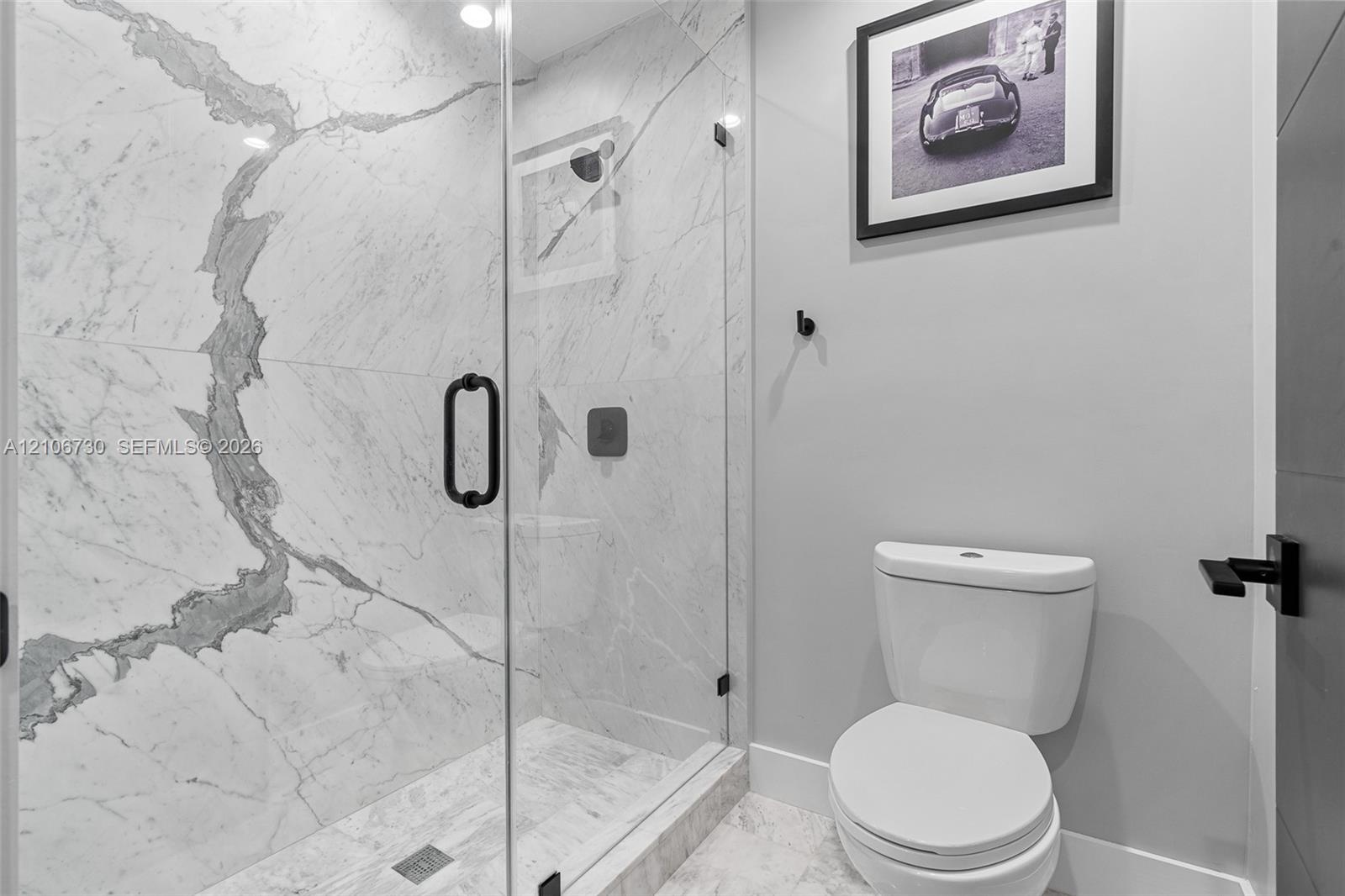 Walk-in shower featuring large-format stone-patterned tile, frameless glass enclosure, and matte black hardware, accompanied by a vitreous china toile