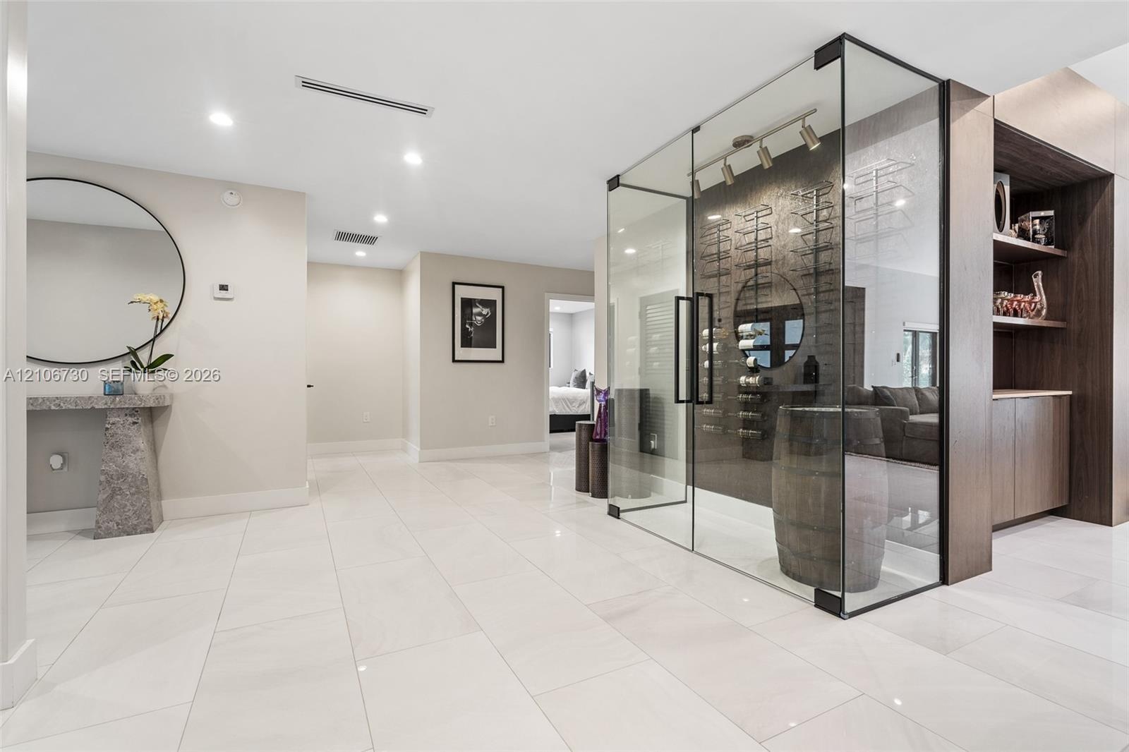 Glass-enclosed temperature-controlled wine display with wall-mounted racking, large-format tile flooring, recessed ceiling lighting, and built-in dark