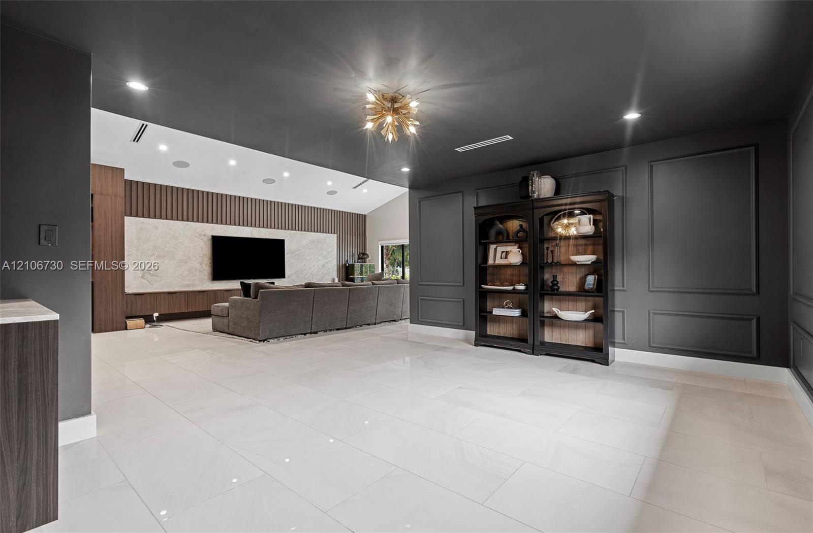 Large format tile flooring, charcoal-painted walls with decorative wainscoting, statement gold-tone ceiling fixture, recessed lighting, and a custom m