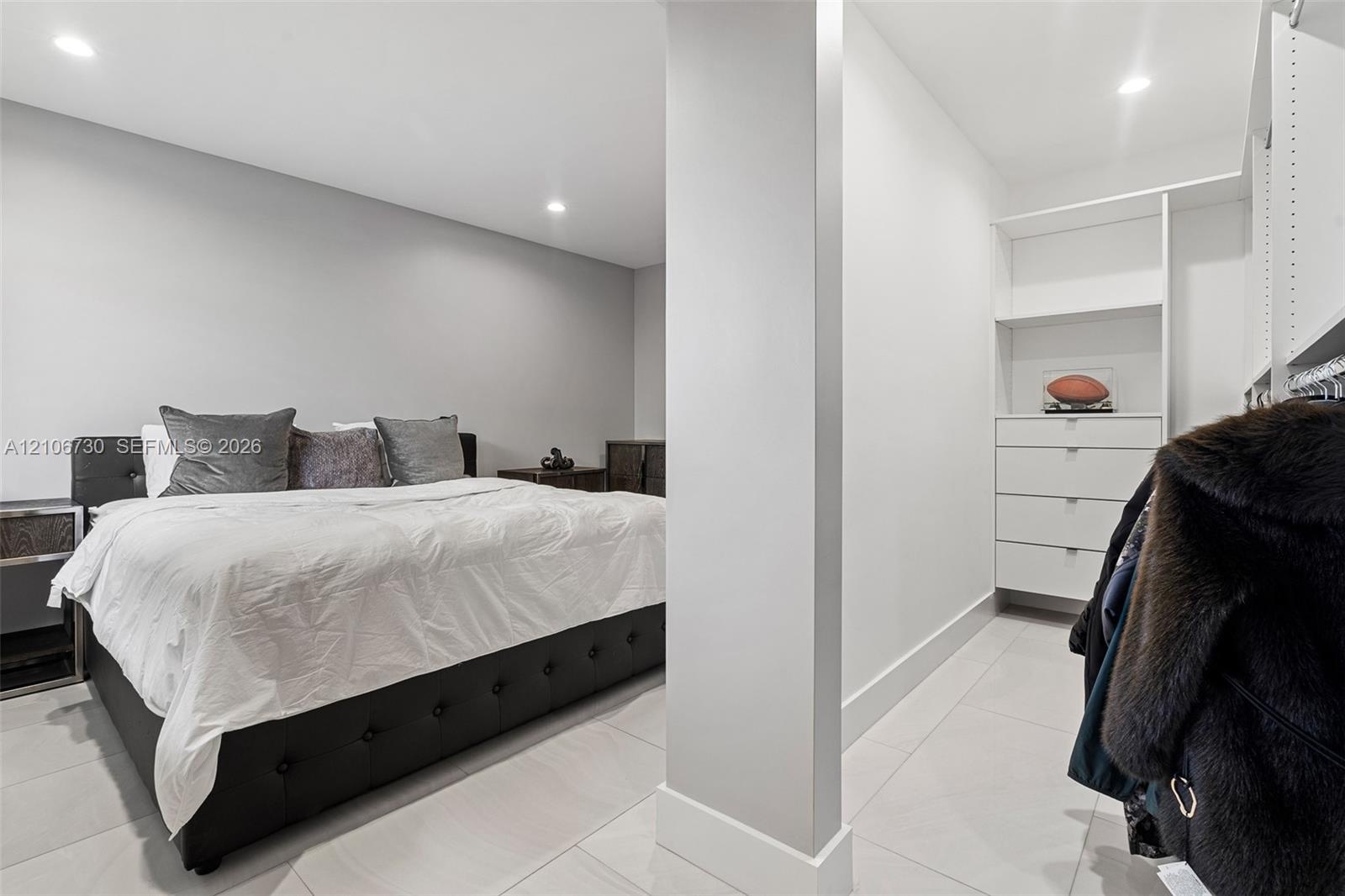 Neutral interior featuring large-format tile flooring, recessed lighting, and built-in closet organization system with integrated drawers and shelving