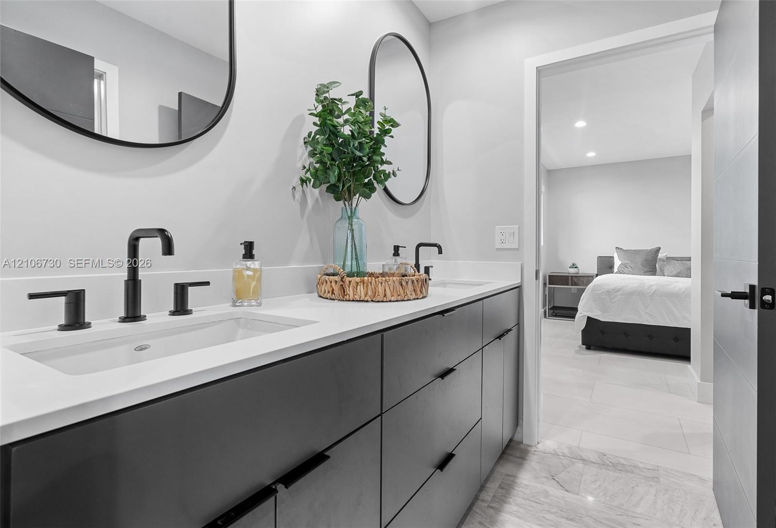 Double vanity with charcoal-toned cabinetry, light-toned stone-surface countertop, dual rectangular undermount sinks, matte black plumbing fixtures, a
