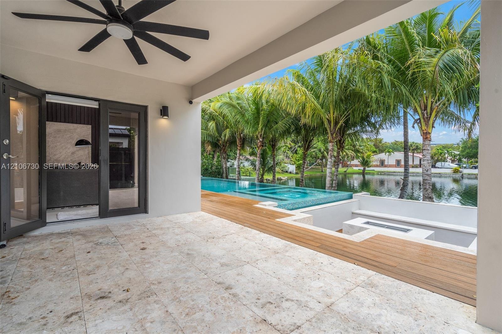 Covered patio featuring stone tile flooring and a ceiling fan, wood-finish decking, sunken seating area with a built-in fire feature, and an infinity-
