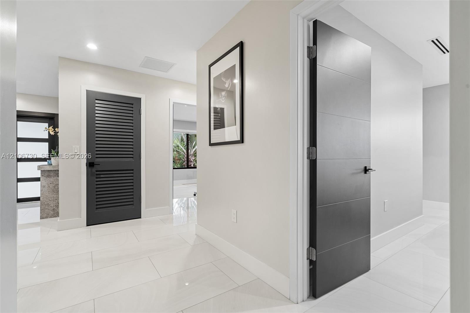 Interior hallway featuring polished large-format tile flooring, matte black lever hardware, a louvered charcoal-finished door, and a multi-panel charc
