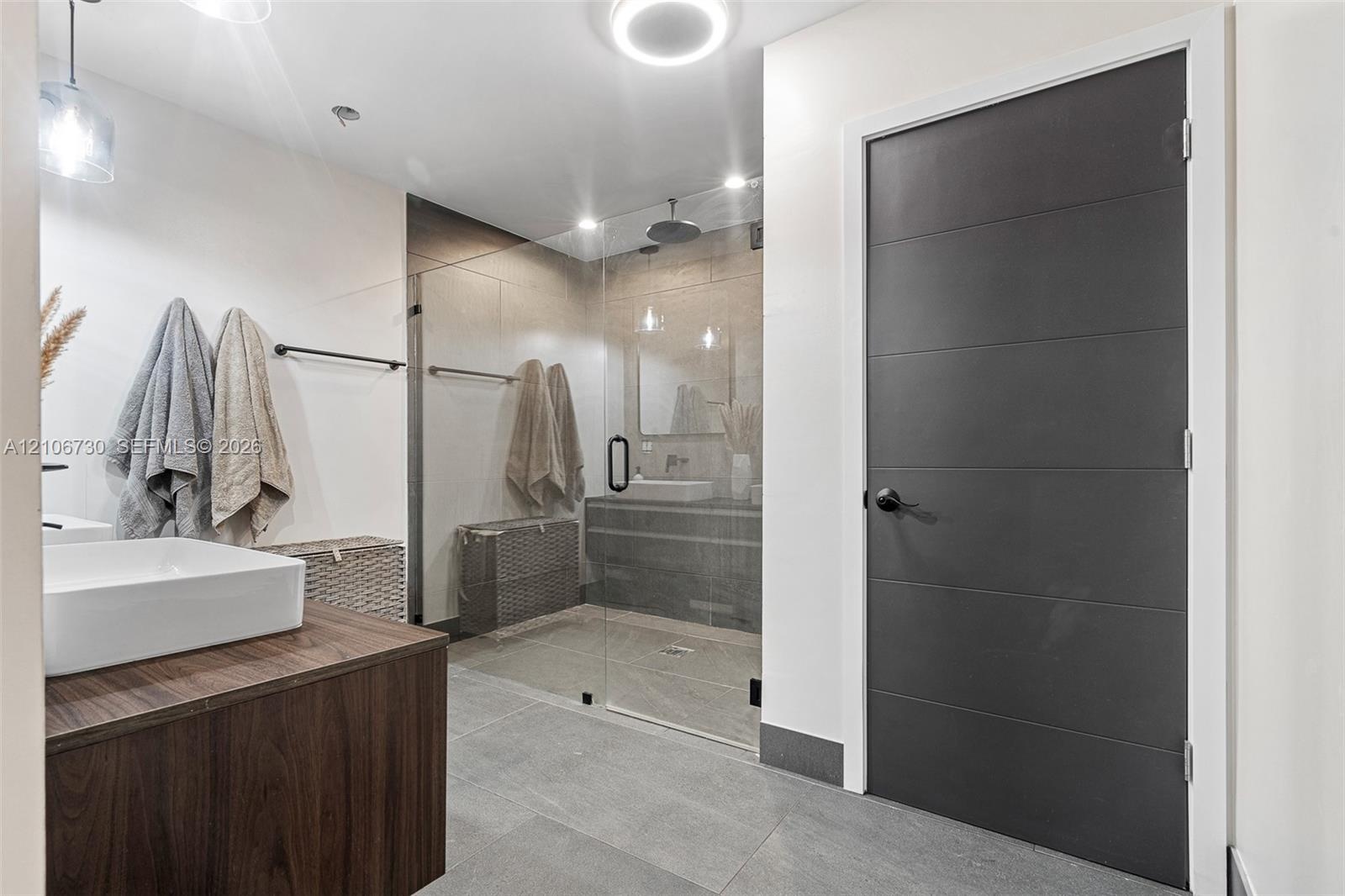 Bathroom featuring a wood-finish vanity with a white vessel sink, large-format tile flooring, a glass-enclosed walk-in shower, and a matte black hardw