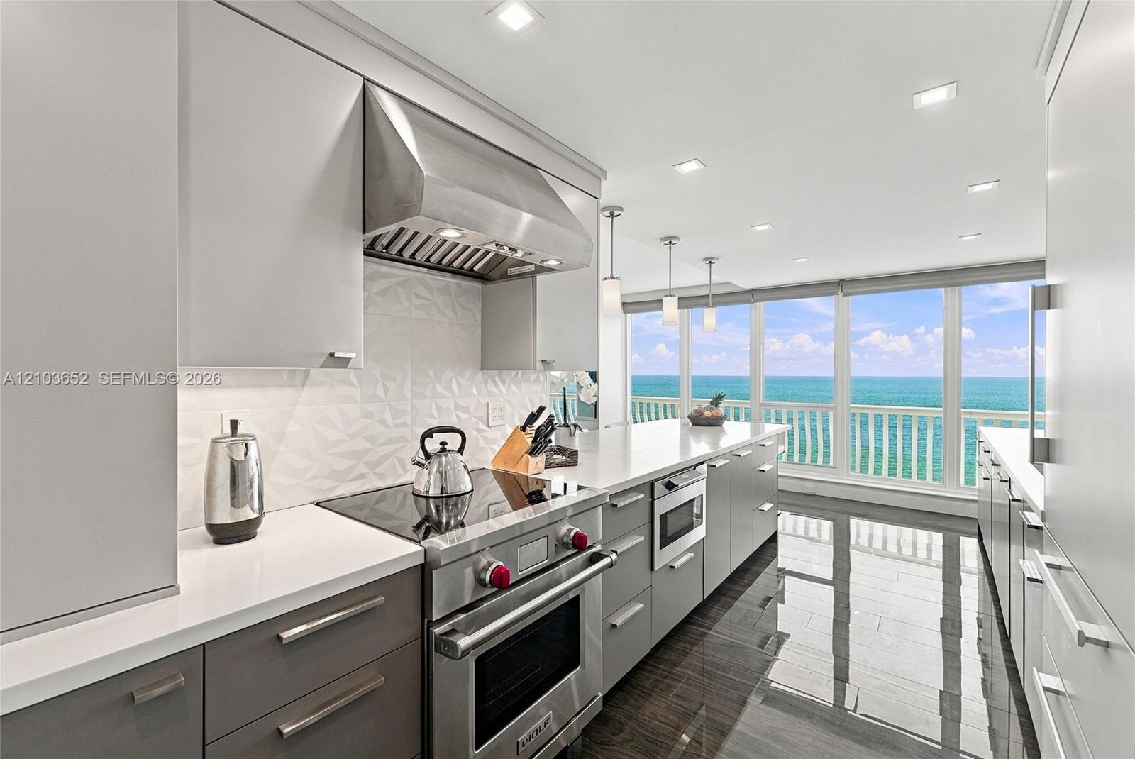 Modern kitchen featuring sleek two-tone cabinetry, professional-grade stainless steel range, geometric tile backsplash, stone countertops, and floor-t
