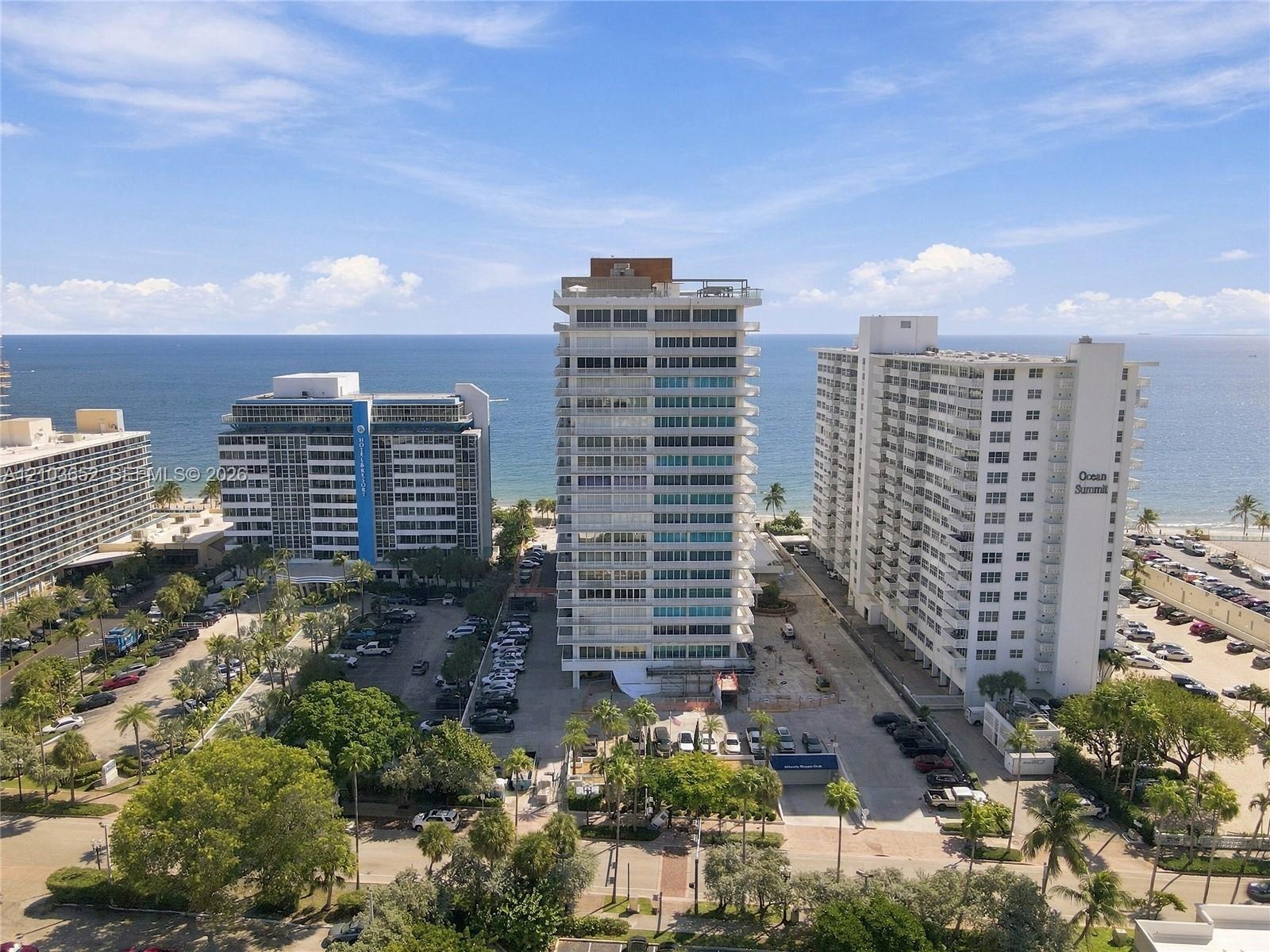Aerial perspective of coastal high-rise properties featuring direct ocean frontage, structured surface parking, and mature palm landscaping