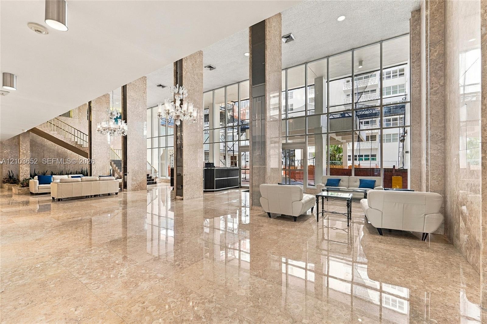 Expansive lobby featuring polished stone flooring, floor-to-ceiling glass walls, decorative chandeliers, and full-height stone-clad columns