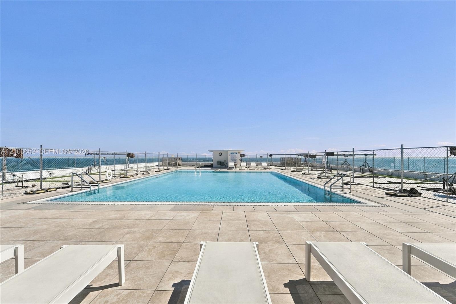 Rooftop swimming pool featuring large-format tile decking, metal perimeter fencing, and stainless steel pool ladders