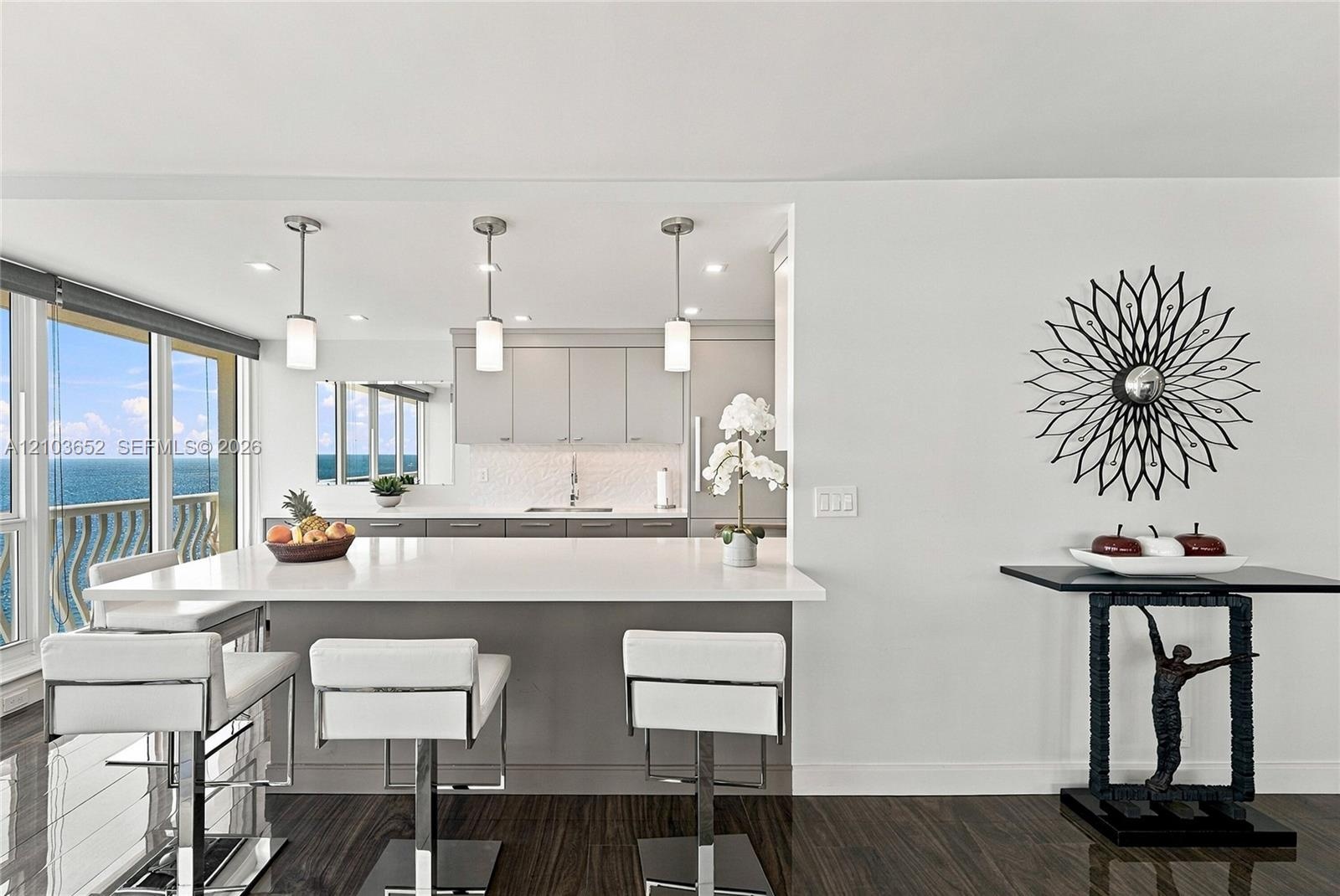 Kitchen featuring a waterfall-edge island with seating, grey cabinetry, textured backsplash, and three cylindrical pendant lights, finished with dark 