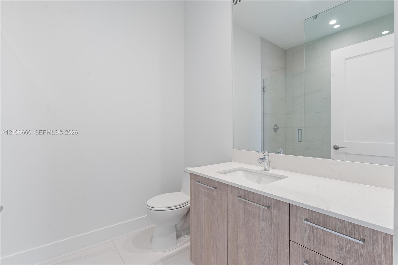 Bathroom featuring a vanity with wood-finish cabinetry, light-toned countertop, undermount sink, large wall-mounted mirror, and glass-enclosed shower