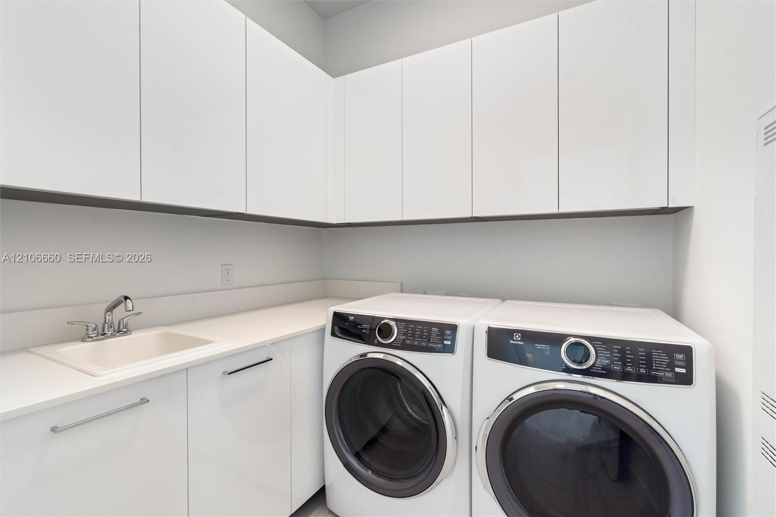 Laundry area featuring high-gloss white upper and lower cabinetry, solid surface countertop, and an integrated basin with a chrome faucet