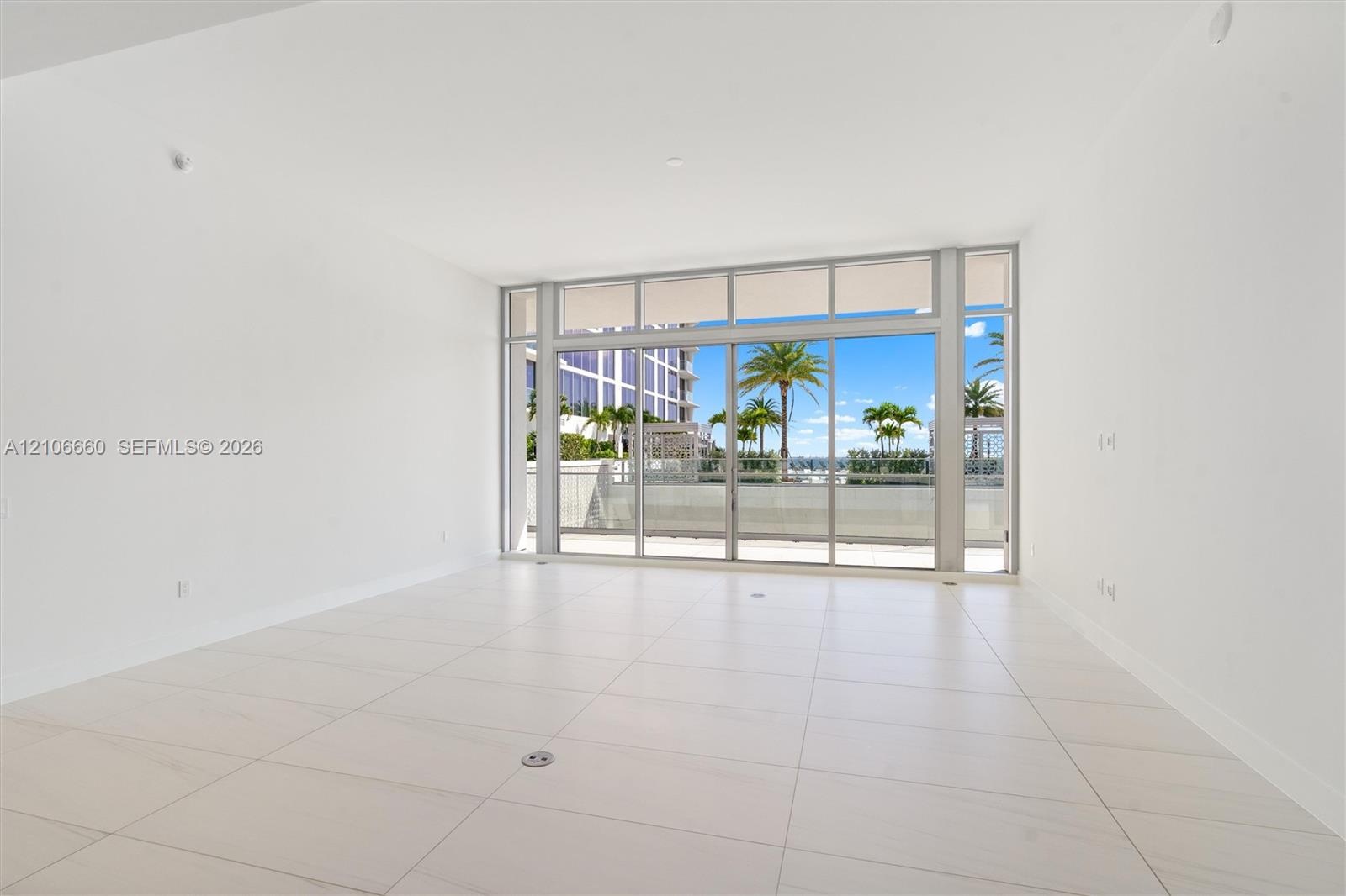 Open-concept interior featuring large-format tile flooring, floor-to-ceiling glass wall, and sliding glass doors leading to an exterior balcony