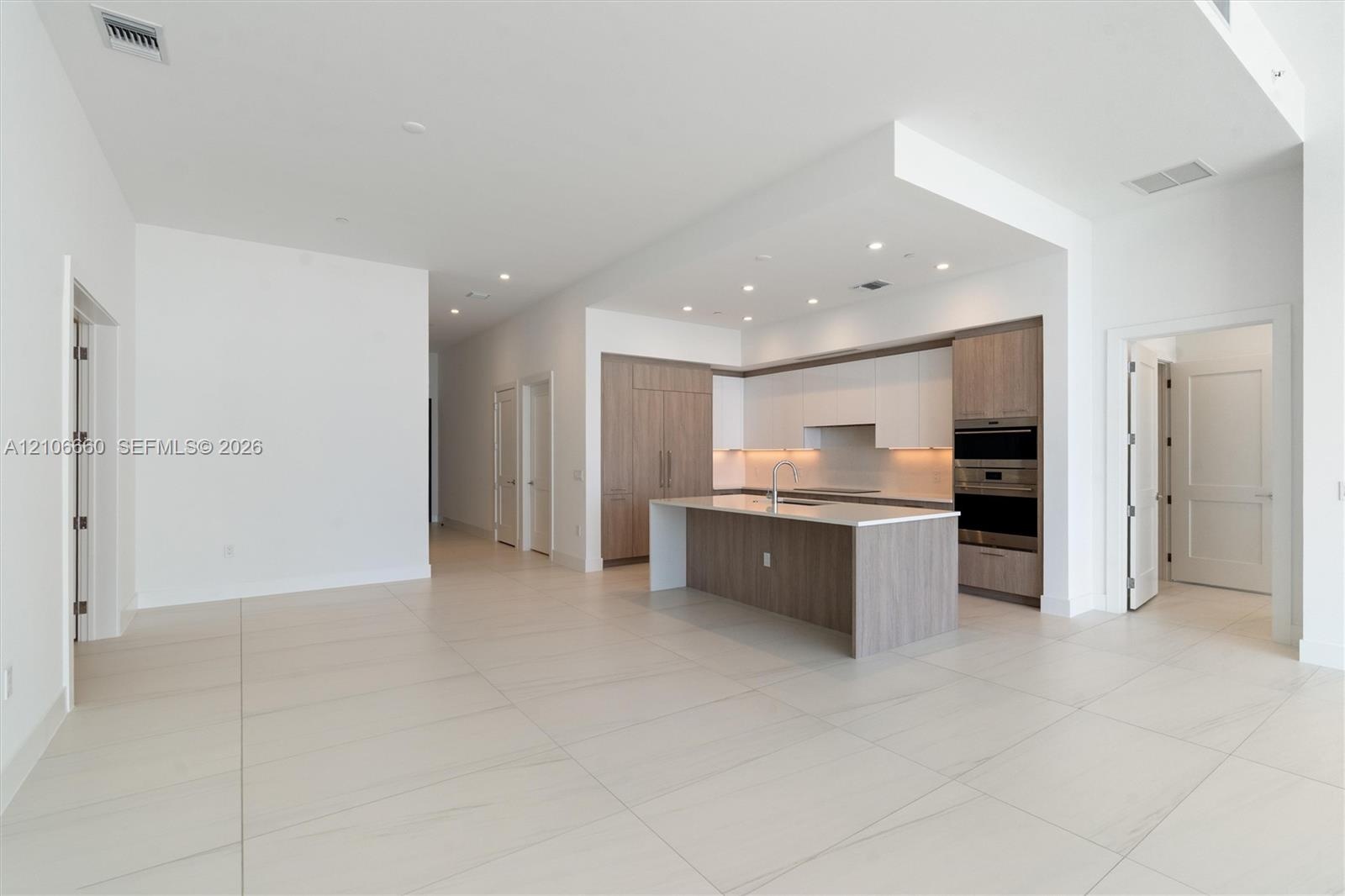 Open-concept kitchen featuring two-toned cabinetry, stone-finish countertops, a central island with an integrated sink, built-in stainless steel appli