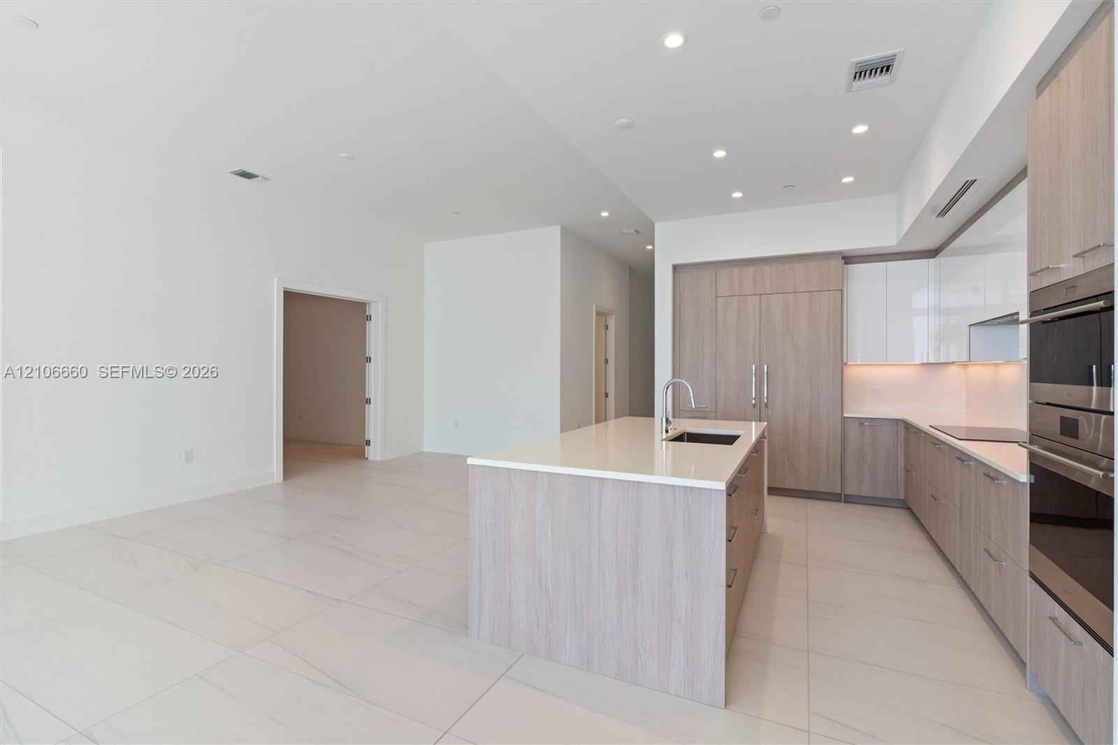 Kitchen featuring wood-finish cabinetry, white high-gloss upper cabinets, solid-surface countertops, large kitchen island with integrated sink, and bu