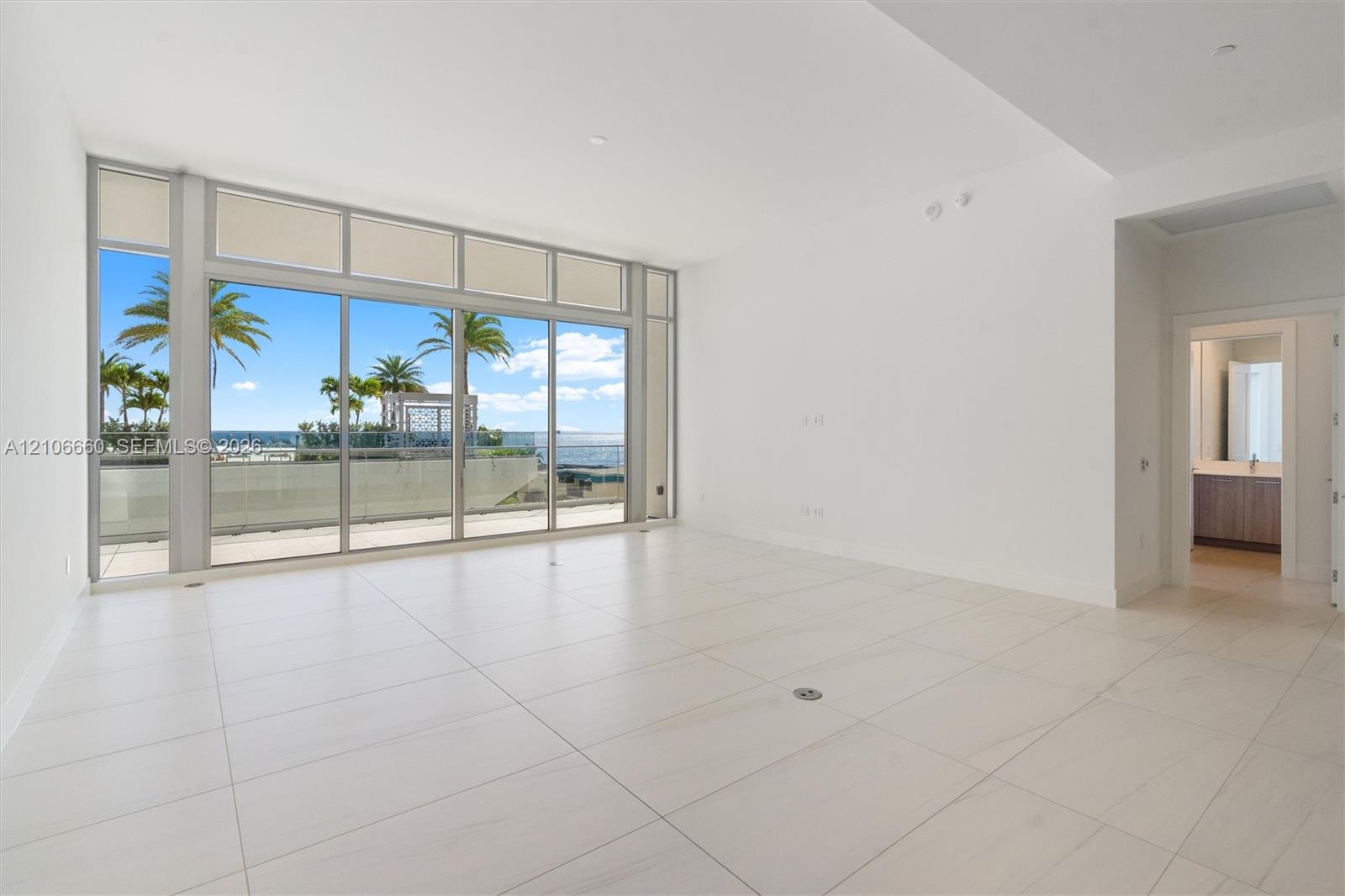Floor-to-ceiling glass wall with sliding doors, large-format tile flooring, recessed ceiling lighting, and exterior balcony