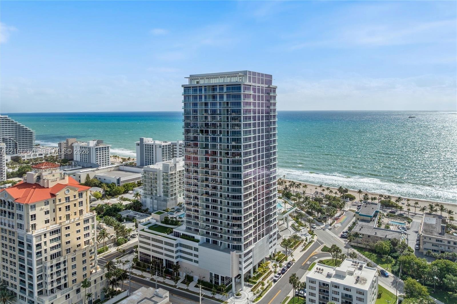 High-rise residential tower featuring a glass-facade exterior, wrap-around balconies, and a multi-level parking structure