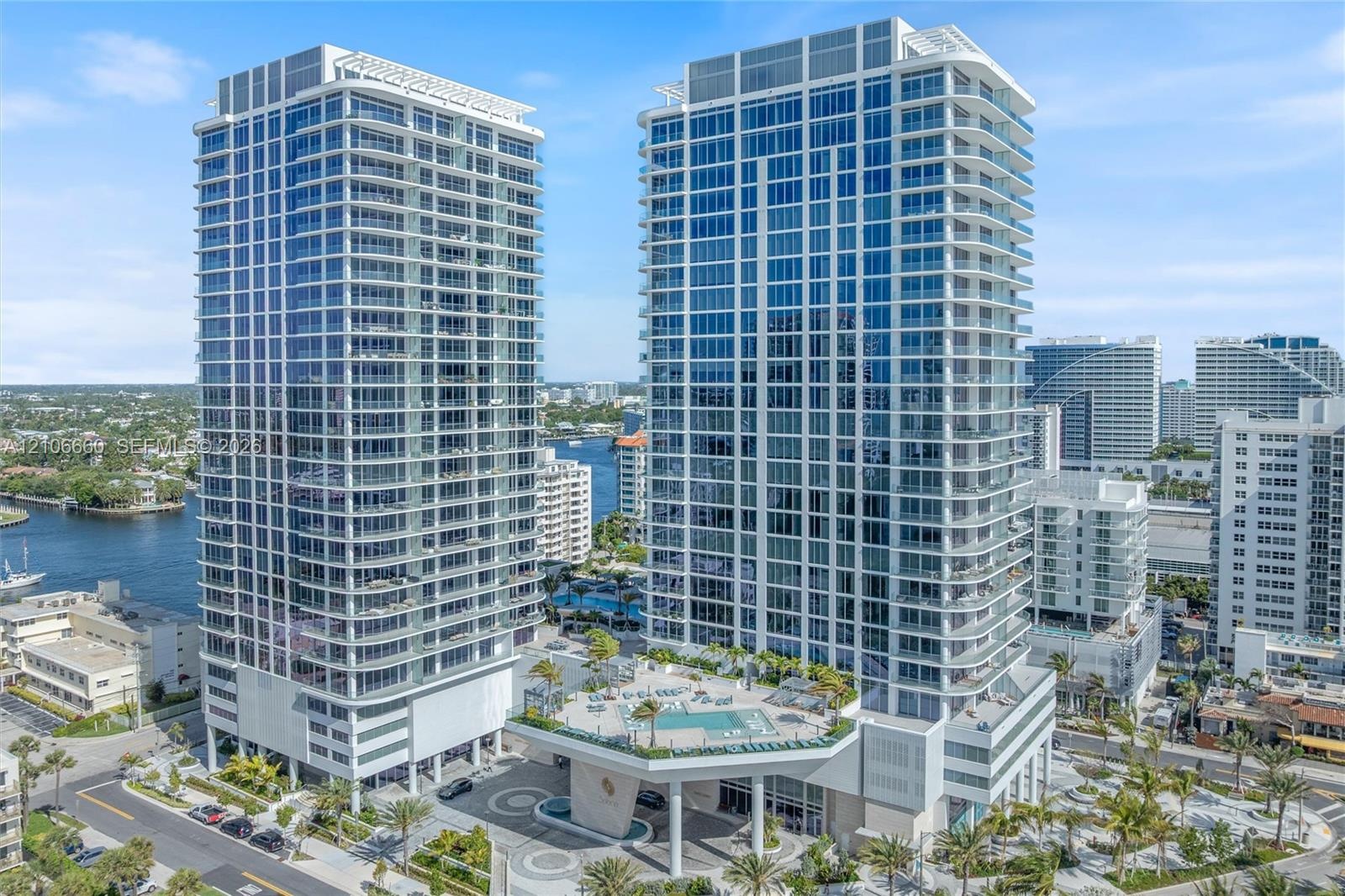High-rise residential towers featuring floor-to-ceiling glass paneling, wrap-around balconies, an elevated podium pool deck, and structured covered en
