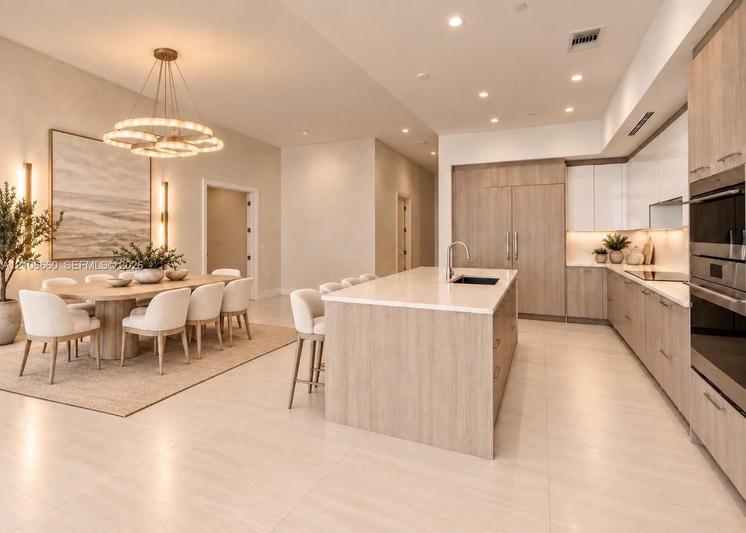 Kitchen featuring light wood-finish cabinetry, a large central island with light-toned countertops, integrated stainless steel appliances, recessed li