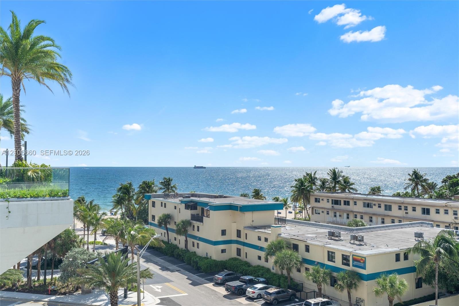 Oceanfront setting featuring a glass-panel balcony railing, mature palm trees, and expansive coastal exposure