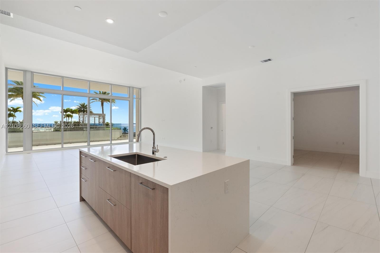 Kitchen island featuring stone countertops, a stainless steel undermount sink, and wood-finish cabinetry, set against large floor-to-ceiling windows w