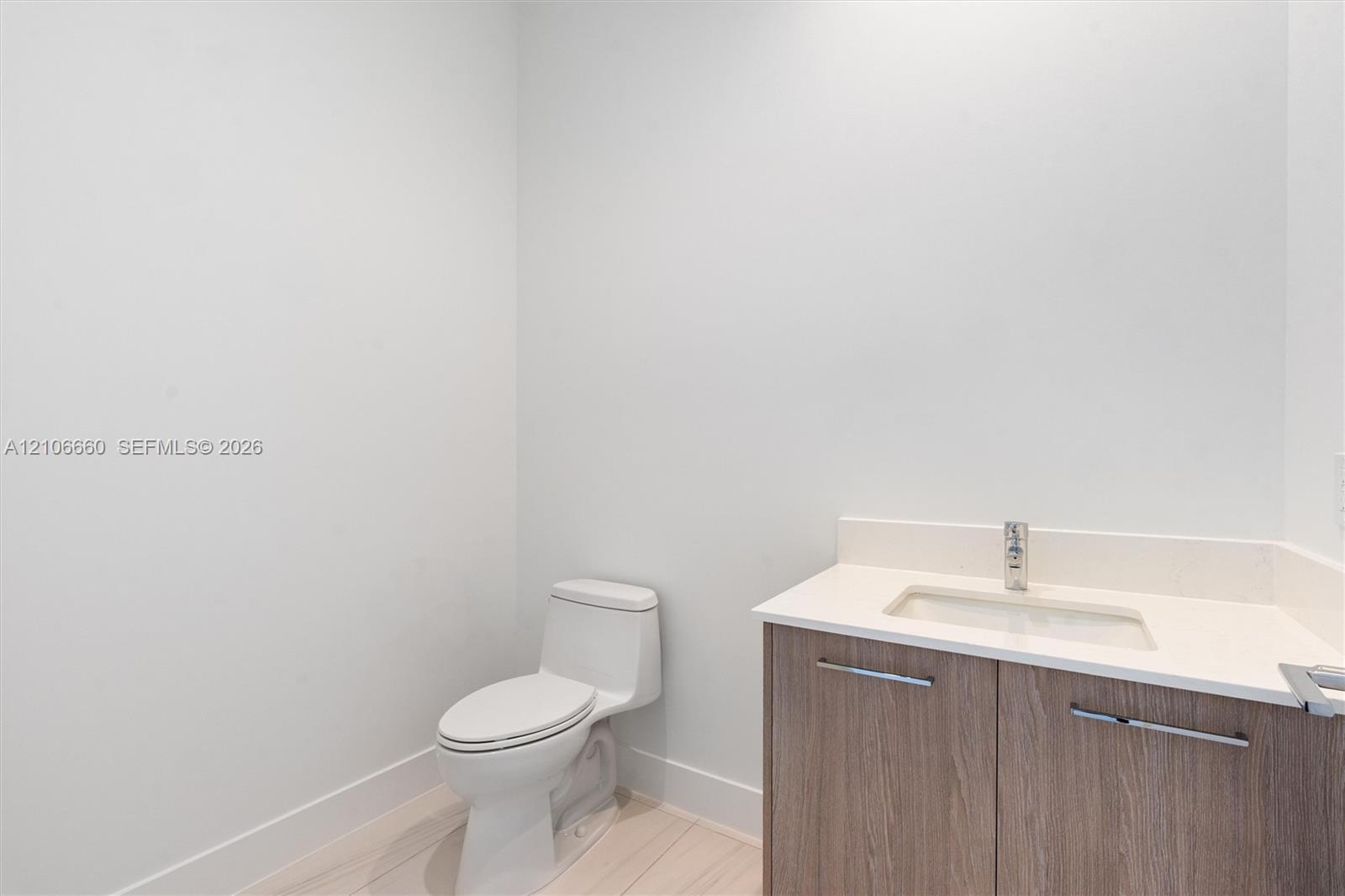 Bathroom featuring a wood-finish vanity with a stone-composite countertop, integrated rectangular sink, chrome-finish faucet, and a one-piece elongate