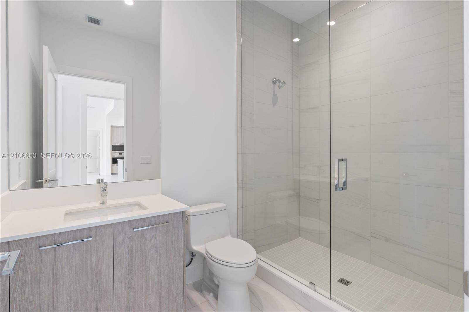 Bathroom featuring a vanity with a white countertop and rectangular undermount sink, a frameless glass-enclosed shower with floor-to-ceiling tile, and