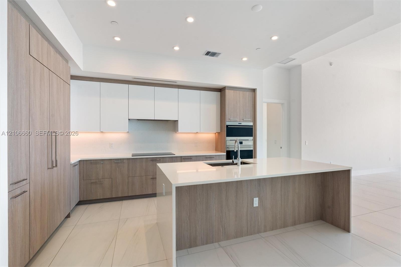 Kitchen featuring two-tone cabinetry with wood-finish and matte white finishes, a large central island with a solid-surface countertop, integrated wal