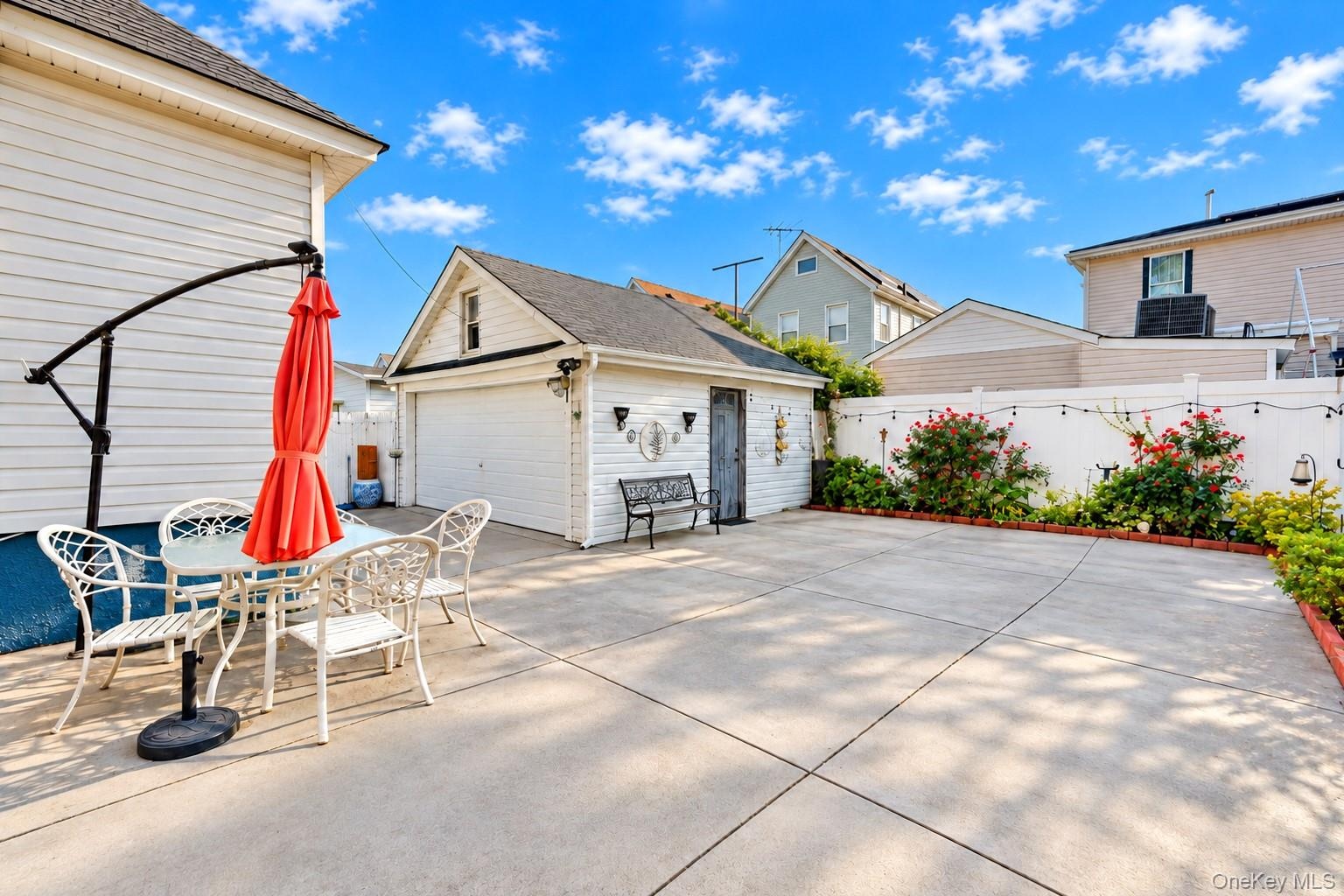 Concrete patio space featuring a detached garage, white vinyl fencing, and established perimeter landscaping