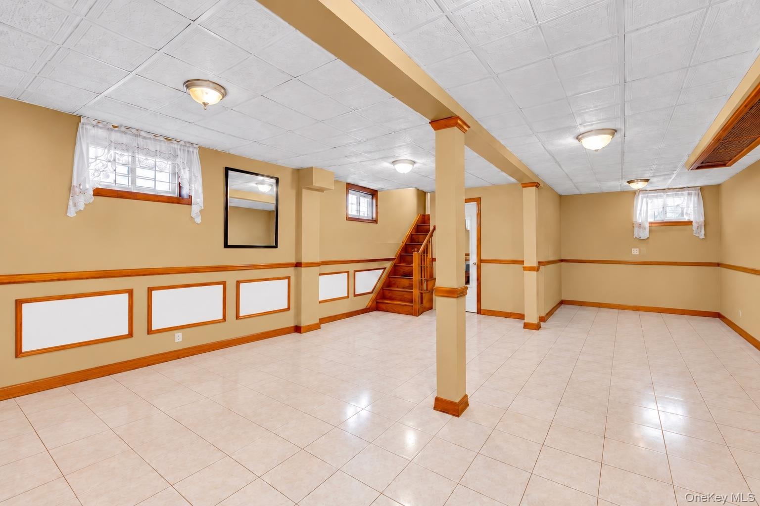 Finished lower-level space featuring tile flooring, wooden chair rail trim, recessed lighting, and a drop ceiling
