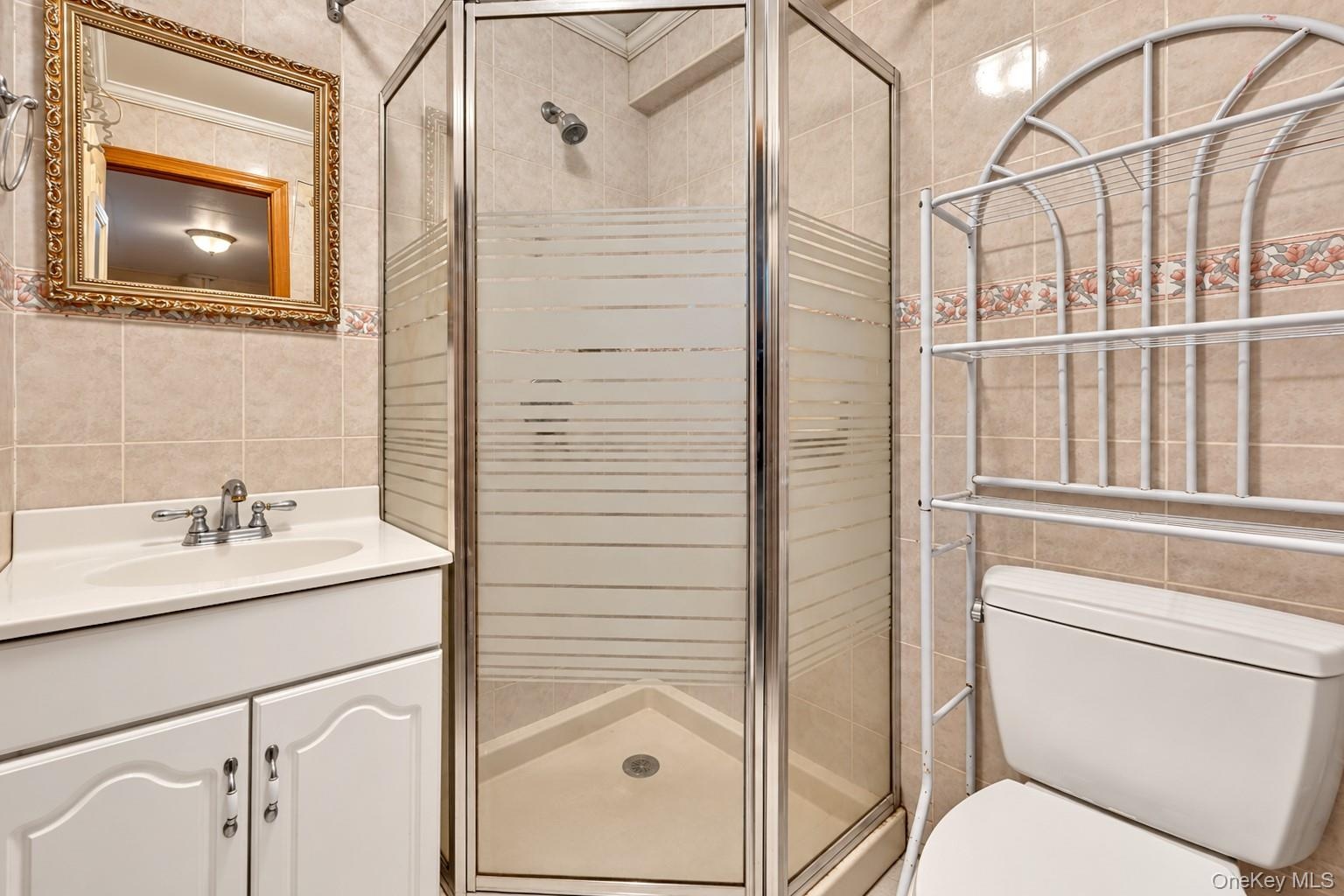 Bathroom featuring a corner shower with glass enclosure, white vanity cabinet, solid-surface countertop with integrated sink, and ceramic wall tiling