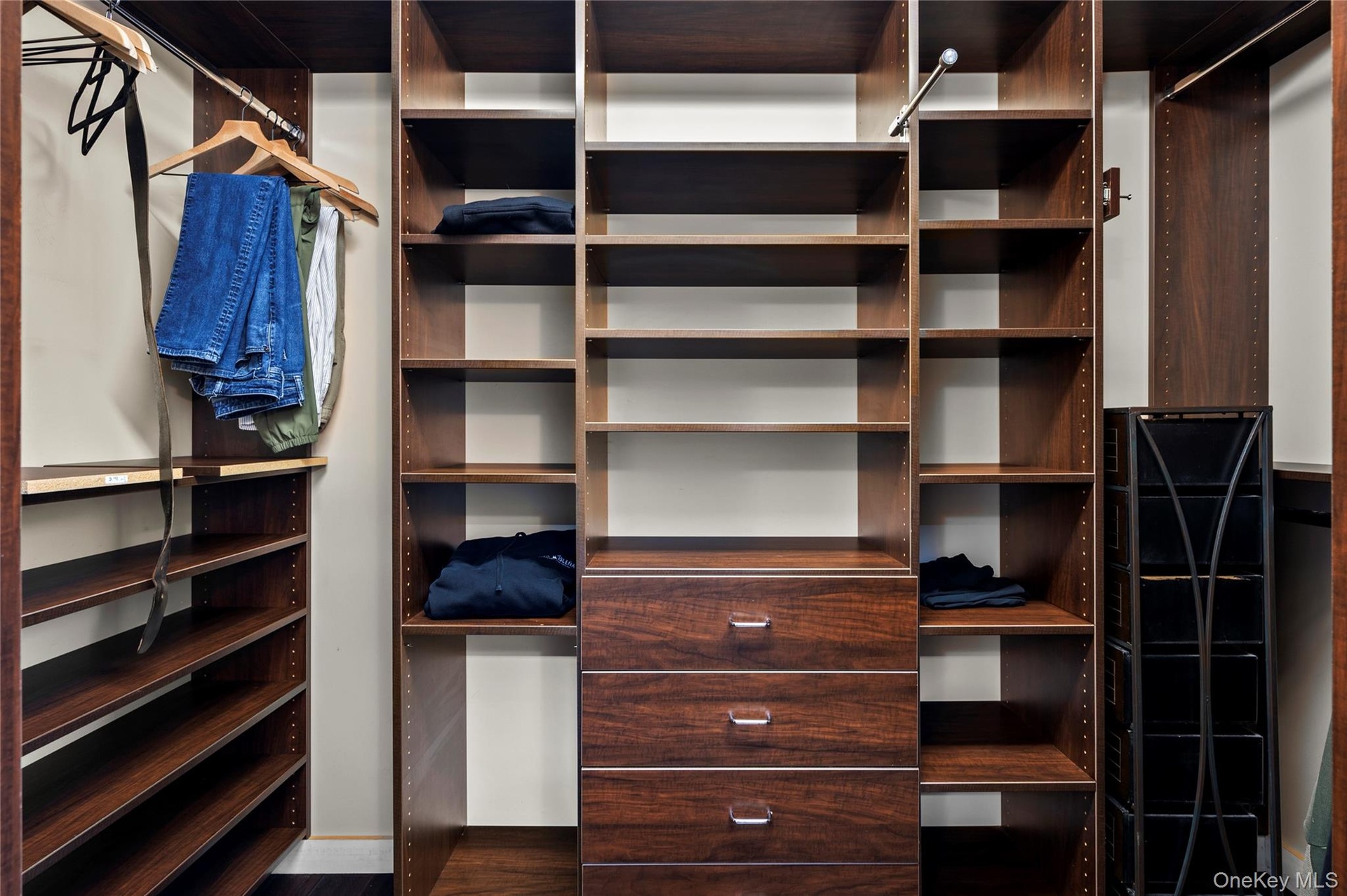 Custom walk-in closet featuring floor-to-ceiling wood-finish cabinetry, adjustable shelving, integrated hanging rods, and a three-drawer built-in dres