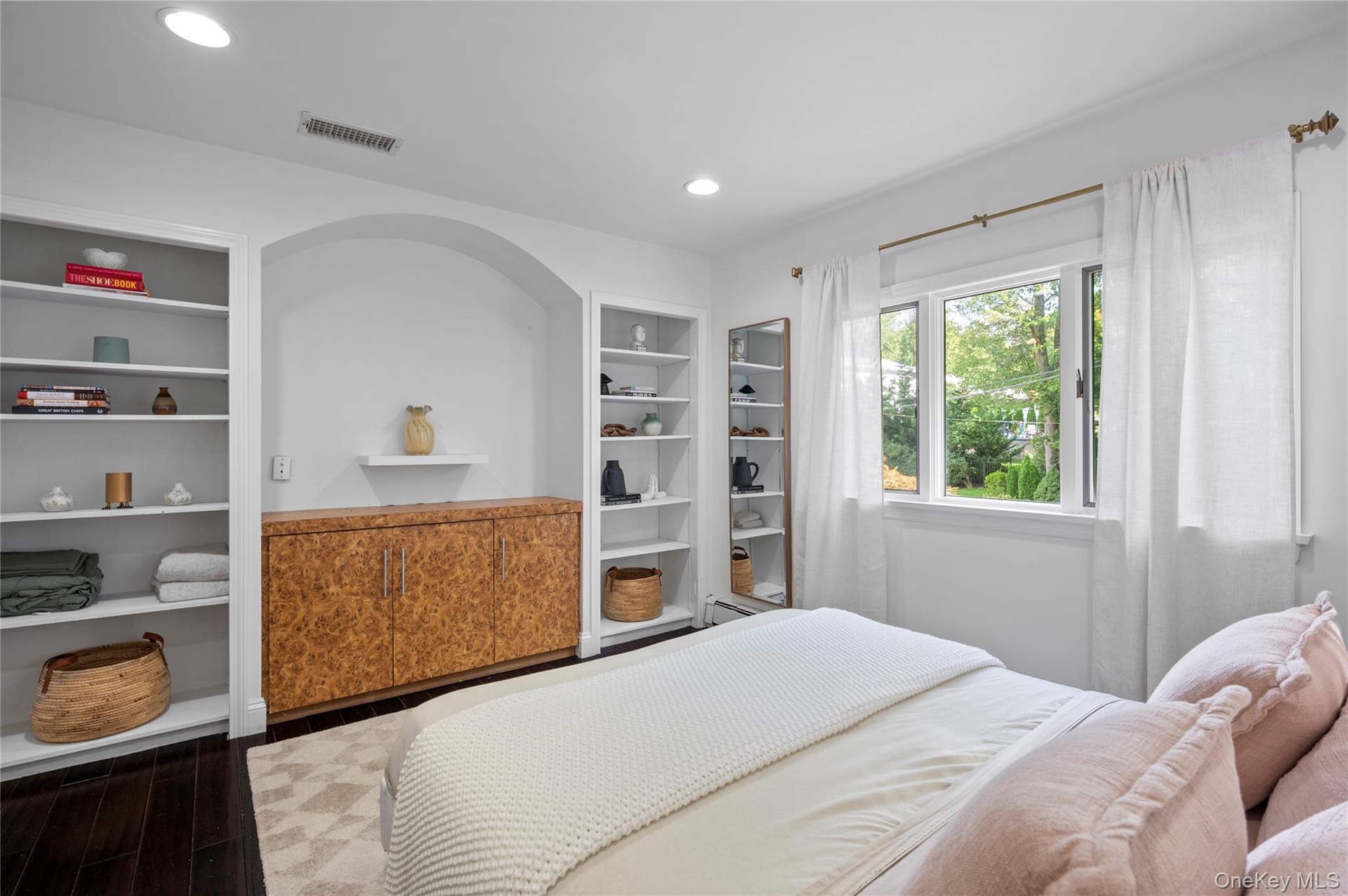 Built-in cabinetry with wood-grain finish, recessed shelving, arched architectural alcove, dark wood-finish flooring, and multi-pane window