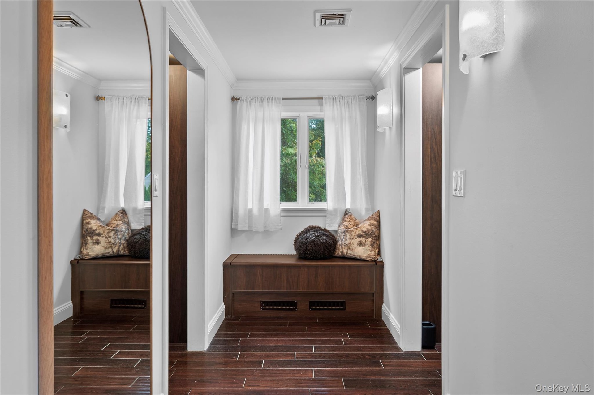 Hardwood-style flooring, built-in wooden cabinetry, arched wall mirror, wall-mounted sconce lighting, and crown molding