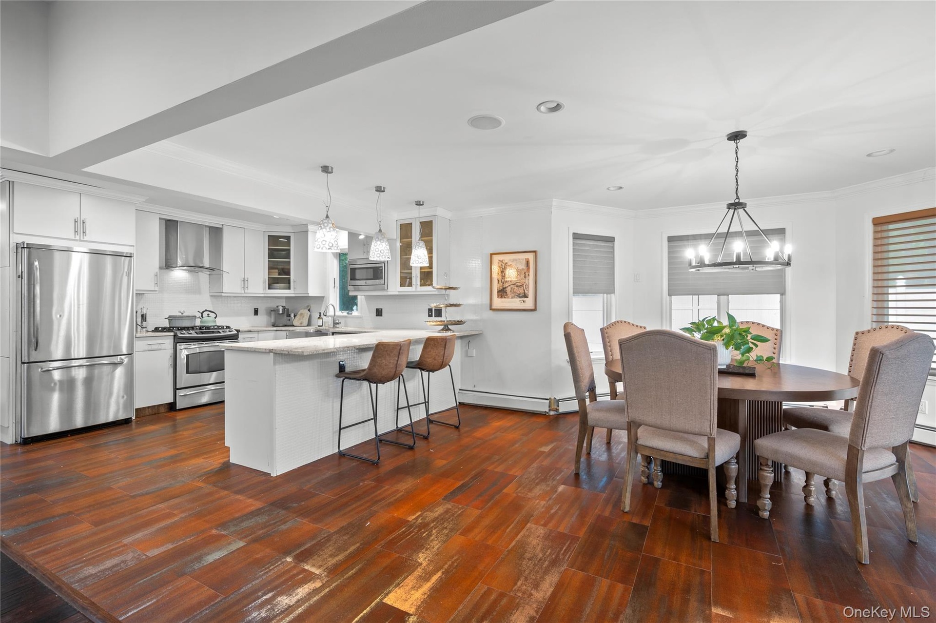 Kitchen featuring wood-finish flooring, white cabinetry, stone-surfaced kitchen island, stainless steel appliances, and multi-light hanging fixtures
