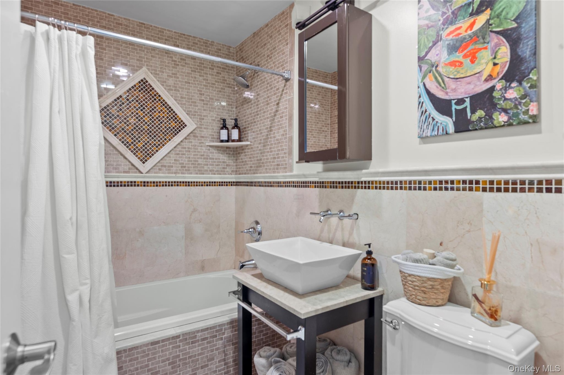 Bathroom featuring a vanity with a rectangular vessel sink, stone countertop, tiled tub surround with decorative mosaic inlay, and a wall-mounted medi