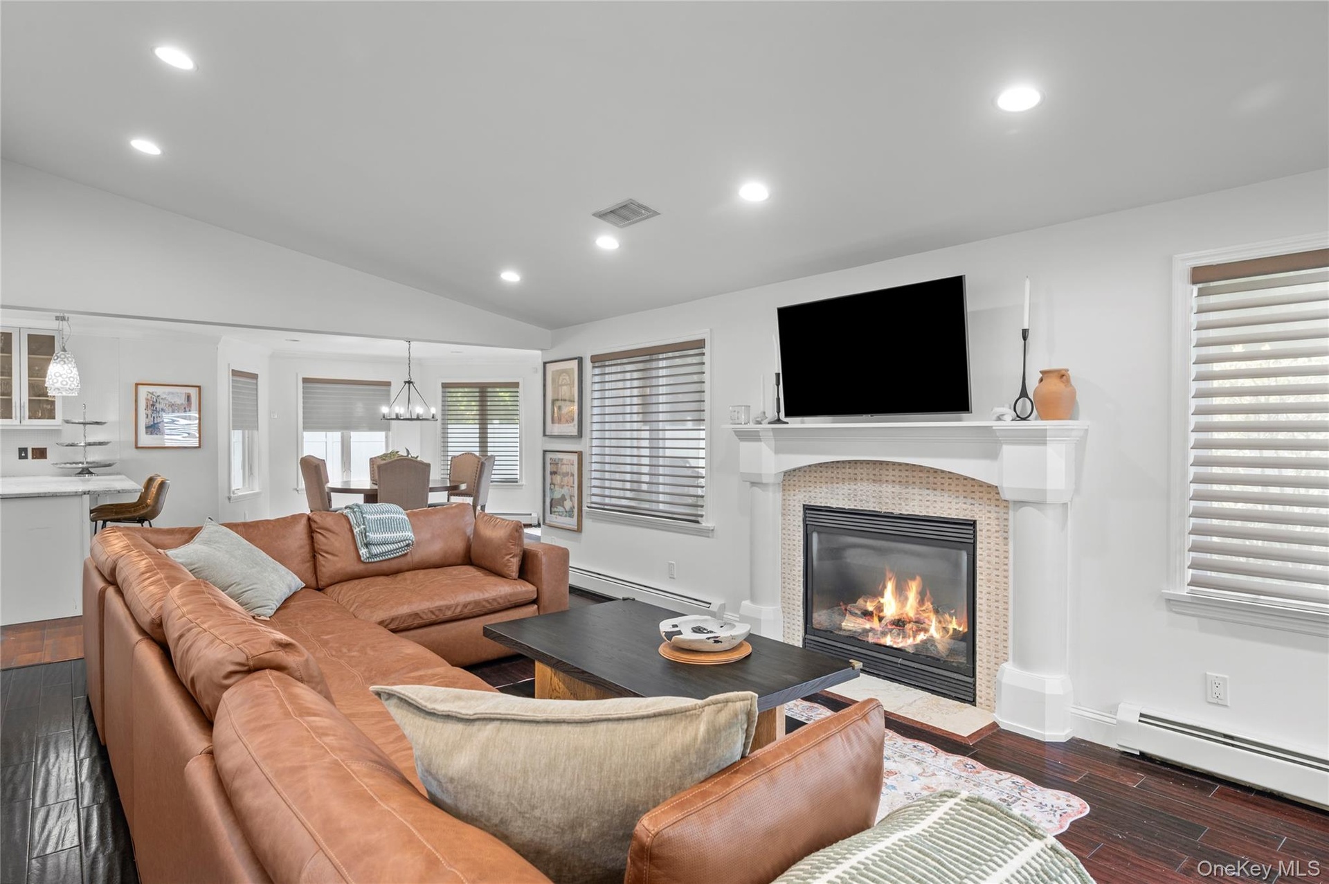 Vaulted ceilings with recessed lighting, dark wood-finish flooring, and a fireplace featuring a detailed mantel, tiled surround, and column accents