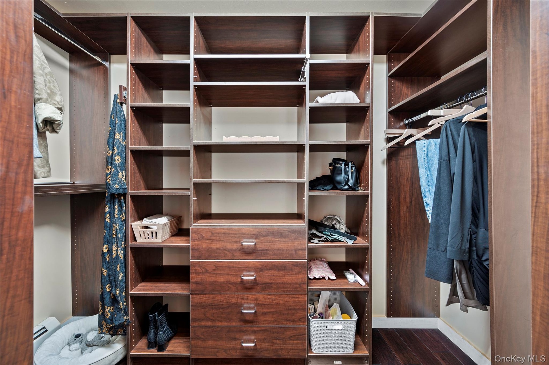 Custom walk-in closet featuring floor-to-ceiling wood-finish cabinetry, extensive shelving, four built-in drawers with hardware, and integrated hangin