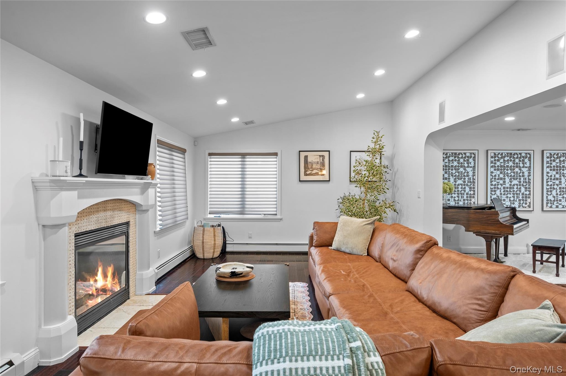 Fireplace with stone-tile surround, mantel, and architectural columns, complemented by recessed lighting, wood-finish flooring, and windows with integ
