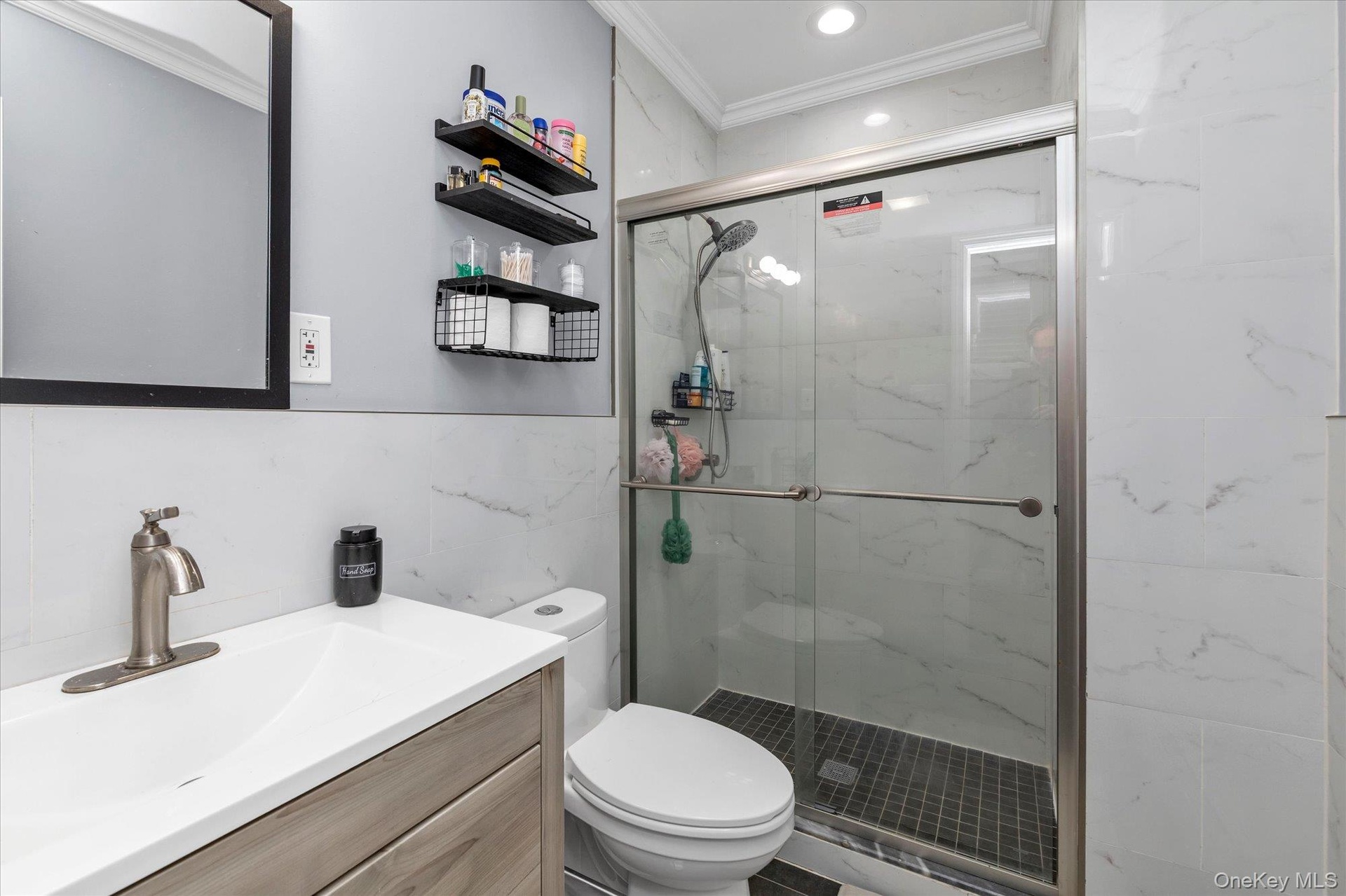 Bathroom featuring a wood-finish vanity with a rectangular sink, brushed nickel faucet, walk-in shower with sliding glass doors, dark tile shower floo