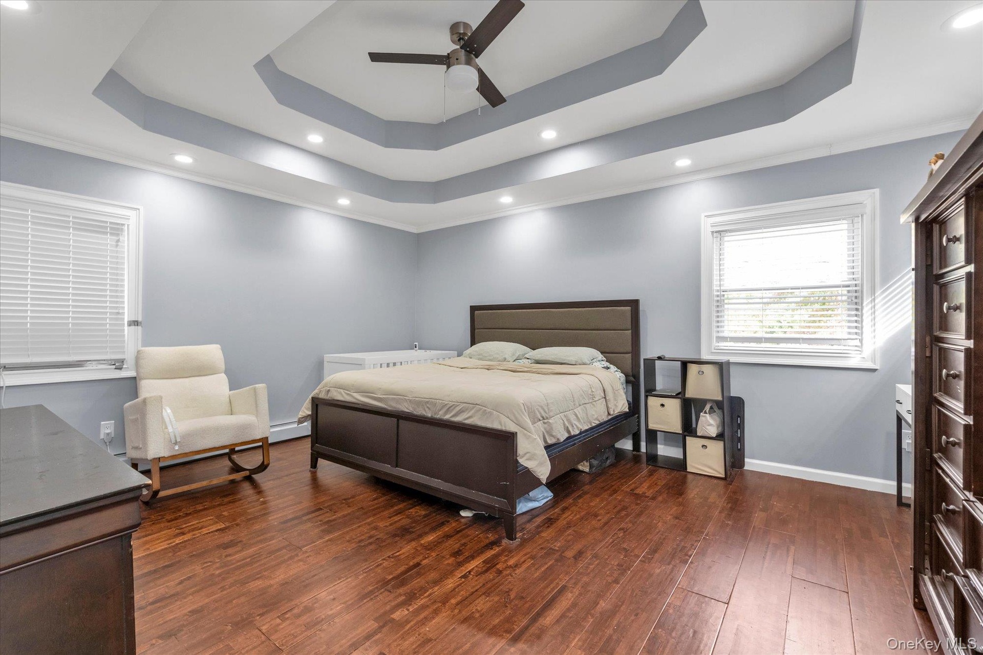 Tray ceiling with recessed lighting, multi-blade ceiling fan, and wood-finish flooring